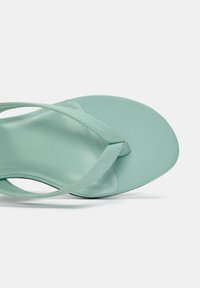 Infradito verde menta con un plantare liscio e lucido e sottili strappi. Le cinghie presentano un design incrociato, offrendo una copertura minimale.