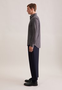 Marineblauw gestreept shirt van lichtgewicht stof, met een button-down kraag en lange mouwen, gecombineerd met donkere broek en zwarte schoenen.