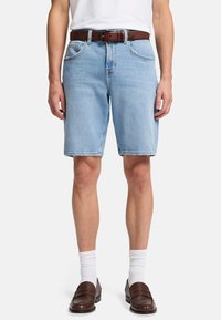 Lyseblå denimshorts med lige skæring, fem lomme-design og synlige syninger. Båret med et brunt læderbælte og brune loafers.