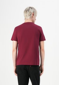 Burgunderfarvet t-shirt med korte ærmer lavet af bomuld, med rund hals og lige snit; båret med sorte jeans. Minimalistisk design.