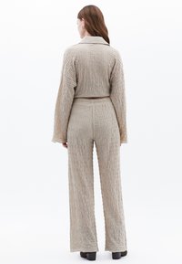 Beige geweven tweedelig outfit met textuurstof, gekraagde cropped top en wijde broek, met subtiele verticale lijnen en een relaxte pasvorm.