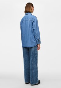 Denim overshirt z ohlapnim krojem, z ovratnikom, dolgimi rokavi in ukrivljenim robom. Svetlo do srednje modra odtenek z zbledelim vzorcem.
