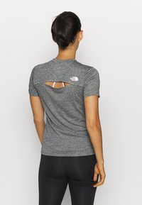 Gray short-sleeve athletic shirt with a back cutout, featuring a white logo on the upper left. Paired with black leggings.