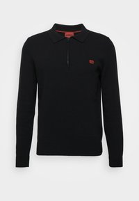 Czarny dziergany sweter polo z ćwierć zamkiem, ribbowymi mankietami i małym czerwonym logo na piersi. Posiada jednolitą fakturę i klasyczny design.