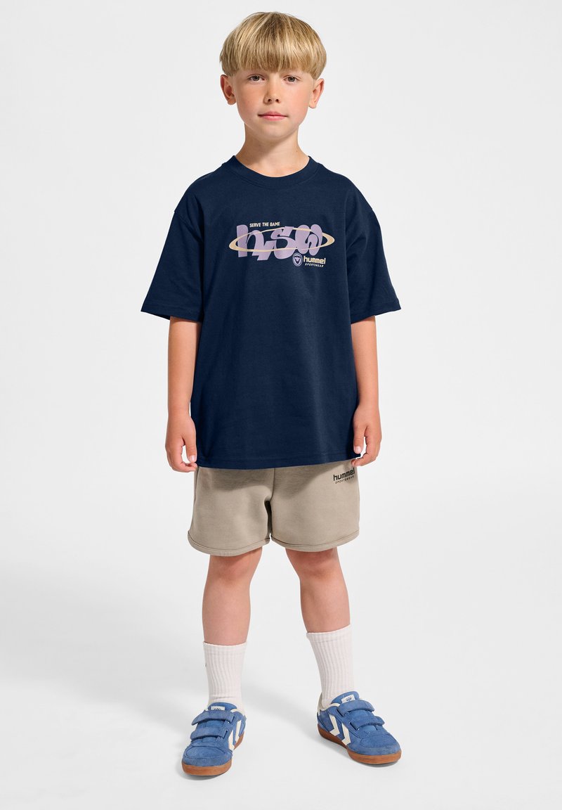 Mörkblå bomulls-T-shirt med korta ärmar och grafisk tryck; kombinerad med beige shorts och blå sneakers med kardborreband.