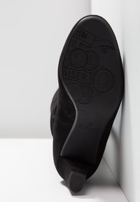 Bottine en daim noir avec semelle embossée présentant des motifs de pièces de monnaie et l'inscription "Peter Kaiser Germany depuis 1838".