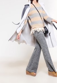 Grauer gestreifter Pullover mit gefiedertem Saum, graue ausgestellte Hose und ein hellgrauer Mantel. Braune Plateauschuhe runden das Outfit ab.