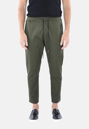 Pantaloni jogger verde oliva con vita elastica e cordoncino, vestibilità affusolata e tasche laterali, abbinati a scarpe nere senza lacci.