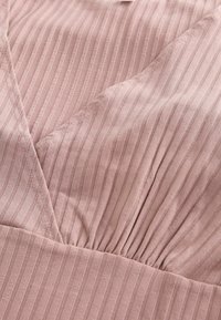 Gros plan sur un tissu côtelé rose doux avec un décolleté en V et un détail de couture froncée.