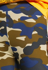 Kamuflasje leggings med nyanser av blått, brunt og beige, med en jevn og elastisk tekstur. Inkluderer distinkte abstrakte mønstre og sømmer.