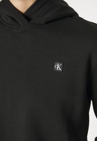 Czarna bluza z kapturem o miękkiej fakturze, z małym wyszywanym logo na piersi. Zaprojektowana z kapturem ze sznurkiem i mankietami.