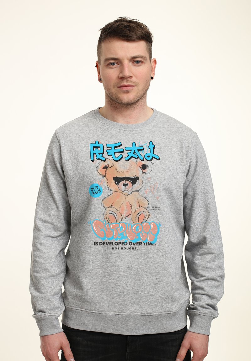 Sudadera gris con un gráfico de un oso de dibujos animados con gafas de sol, texto azul y letras en negrita. Material suave con puños acanalados.