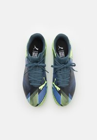 Zapatillas deportivas negras y azules con una parte superior texturizada, acentos verdes y un patrón de rayas dinámico; los cordones son de color azul oscuro e incluyen un código QR.