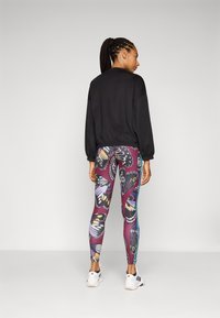Sweatshirt noir court avec des manches ballon associé à des leggings violets à motif de papillons. Modèle portant des chaussures de sport blanches.