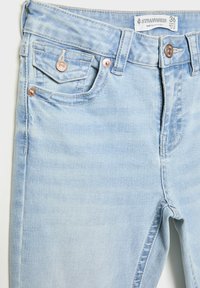 Hellblaue Jeans aus Denim mit verblichenen Bereichen, zwei Vorderentaschen, Kupfernieten und einem Reißverschluss. Das Etikett trägt die Aufschrift "Stradivarius", Größe 36.