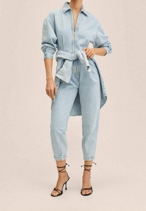 Salopette en denim bleu clair avec un col, des manches longues, une taille cintrée et des chevilles à revers, assortie à des escarpins noirs à lanières.