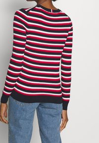 Pull en maille côtelée à manches longues, avec des rayures horizontales bleu marine, rouge et blanc. Col rond classique et tissu extensible.