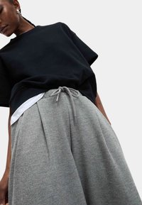 Czarny krótki rękaw sweter o luźnym kroju, założony na białą koszulę, w połączeniu z szarymi spodniami dresowymi z kantem, które mają sznurek w pasie.