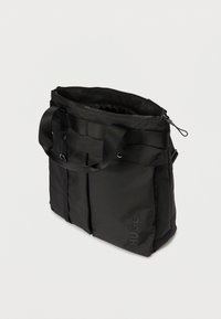 Svart rektangulær tote bag med glidelåsåpning, bærehåndtak, frontlommer og "HUGO"-logo på nederste høyre lomme.