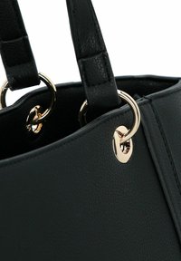 Close-up van zwarte leren handtasriemen, bevestigd met glanzende gouden metalen ringen en rechthoekige gestikte details.