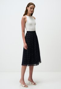 Gonna midi nera plissettata con dettagli argento, abbinata a un top bianco aderente senza maniche. Tacchi aperti bianchi completano il look.