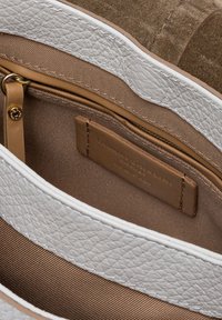 Interno di una borsa in pelle bianca texturizzata con rivestimento in tessuto marrone. Presenta una tasca con zip e un'etichetta impressa con "Gianni Chiarini, Made in Italy."