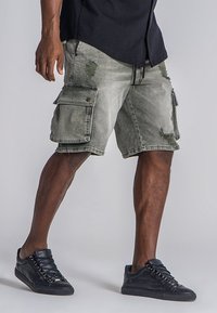 Shorts cargo en denim verde olivo desvaído, con detalles de patchwork y desgaste, múltiples bolsillos laterales y un corte relajado.