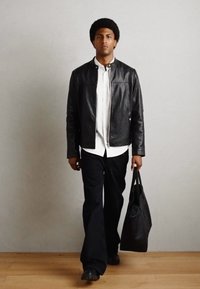 Schwarze Lederjacke, weißes Hemd mit Knöpfen, schwarze gerade Hose und schwarze Tragetasche. Glatte Texturen und minimalistisches Design.