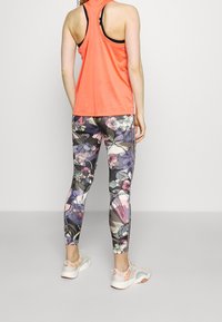 Oranssi urheilutoppi, kukkakuosiset legginsit violeteissa, vaaleanpunaisissa ja harmaissa sävyissä sekä valkoiset lenkkarit, joissa on pastellivärit.