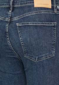 Mörkblå jeans i denim med en strukturerad yta, som har traditionella bakfickor och en läderetikett på midjebandet.