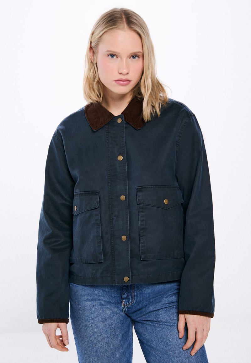 Mörkblå jacka med krage i brunt cordtyg, prydd med guldmetallknappar och två framfickor, designad med en avslappnad passform.