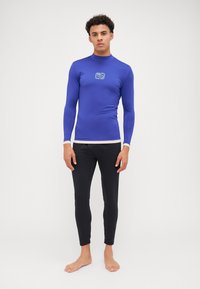 Langermet blå rash guard med høy hals og logo, kombinert med svarte slim-fit badeshorts. Glatt, elastisk stoff, ensartet design.