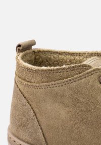 Beige velúr bokacsizma, puha, texturált felülettel. Varrott varrás és húzófül található a száron a könnyű felvétel érdekében.