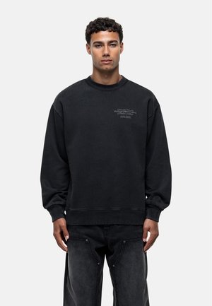 Sweatshirt noir en tissu doux, avec un col rond, des poignets côtelés et un petit logo imprimé sur le devant. Coupe décontractée avec un ourlet droit.