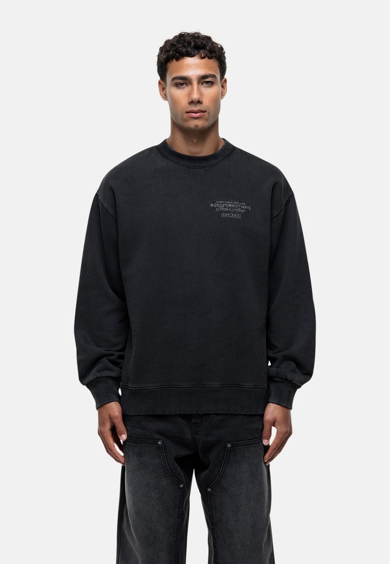 Sweatshirt noir en tissu doux, avec un col rond, des poignets côtelés et un petit logo imprimé sur le devant. Coupe décontractée avec un ourlet droit.