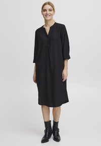 Robe en lin noir avec un décolleté en V, des manches trois-quarts et une patte de boutonnage. Présente des fentes latérales et une coupe décontractée. À associer avec des bottines noires.