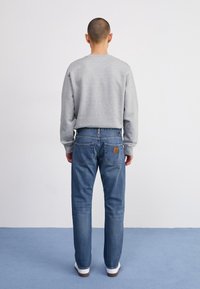Sudadera gris con cuello redondo, combinada con jeans vaqueros azules que tienen bolsillos traseros y una etiqueta de cuero marrón con el logo, zapatillas blancas.