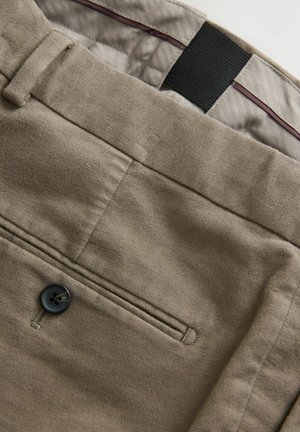 Pantalones beige con cierre de botón, tejido texturizado, un bolsillo frontal con costuras tonales y un patrón de forro interior en contraste.