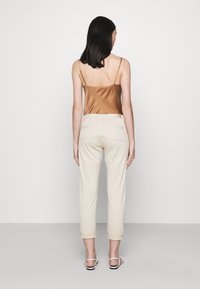 Camiseta de satén marrón con tirantes finos, combinada con pantalones beige enrollados. Diseño sencillo, textura suave y sin patrones ni acentos visibles.