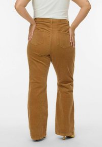 Pantaloni a zampa d'elefante in corduroy marrone con vita alta, dotati di tasche posteriori e un tessuto strutturato. L'orlo è leggermente sfrangiato.