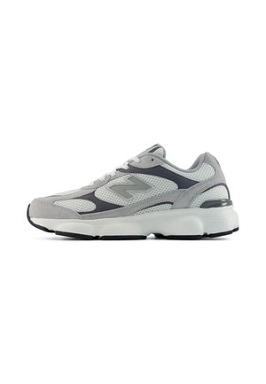Zapatilla deportiva gris y blanca con paneles de malla y ante, suela blanca gruesa y un logotipo estilizado de "N" en el lateral.