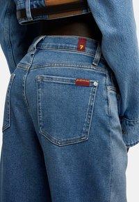 Niebieskie dżinsy z denimu o średnim przetarciu. Charakteryzują się czerwoną metką na pasku oraz tylnej kieszeni. Pięciokieszeniowy krój, trwałe przeszycia.