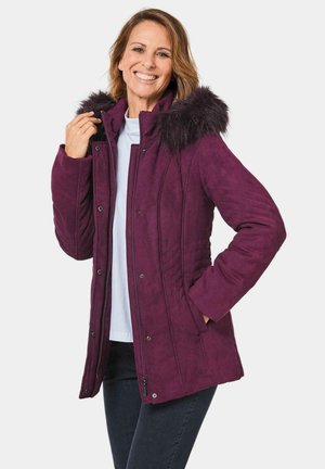 Lila Fake-Suede-Jacke mit abnehmbarer, fellgefütterter Kapuze, gesteppten Details und Fronttaschen, getragen über einem hellen Oberteil.