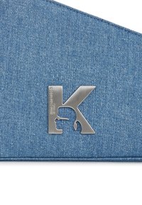 Denim cepure ar metālisku logotipu "K" un silueta detaļām. Audums ir gaiši zils ar smalku tekstūru un šuvju akcentiem.