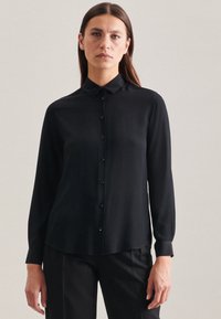 Maglietta nera a maniche lunghe con colletto, chiusura frontale a bottoni e tessuto liscio. Polsini affilati e vestibilità sartoriale visibile.