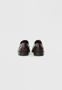 Brown leather shoes with a smooth texture, rounded shape, and a black rubber sole. Minimalist design with no visible hardware or accents.