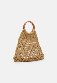 Sac à main macramé tissé en beige avec une forme triangulaire structurée, doté de poignées en boucle en bois et de motifs géométriques ouverts.