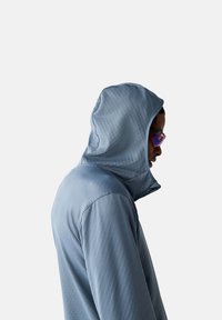 Leichte Kapuzenjacke aus strukturiertem hellblauem Stoff, mit hohem Kragen und glatter Oberfläche, im schrägen Seitenansicht.