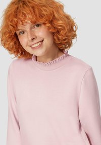 Różowy sweter wykonany z miękkiego materiału, z falbankowym dekoltem, długimi rękawami i luźnym krojem, o gładkiej teksturze i delikatnym połysku.