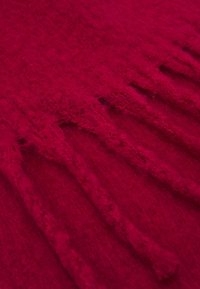 Tissu rouge profond et doux avec des bords frangés montrant des fibres texturées et des détails tissés.